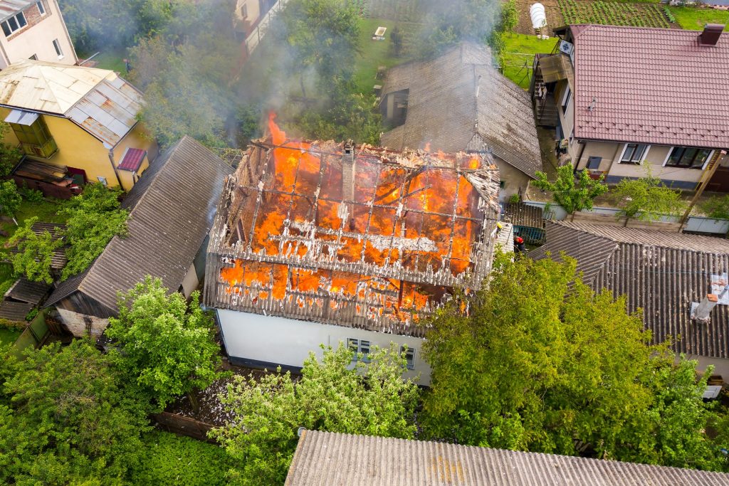 Aerial view of a house on fire with orange flames and white thick smoke