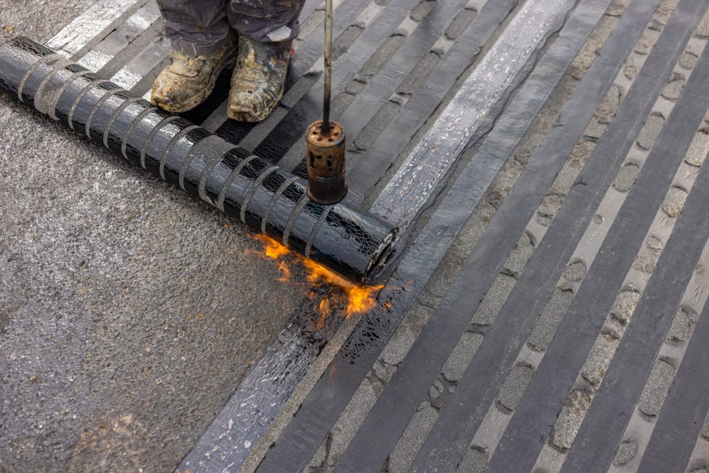 Workers placing a vapor barrier on the roof using a propane gas torch for welding bitumen sheets